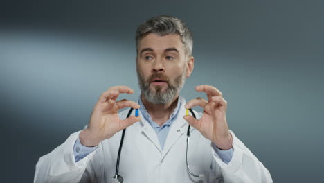 Caucasian-male-physician-holding-two-pills-in-hands,-one-yellow-and-one-blue,-while-comparing-them-and-studying-carefully.-Close-up.
